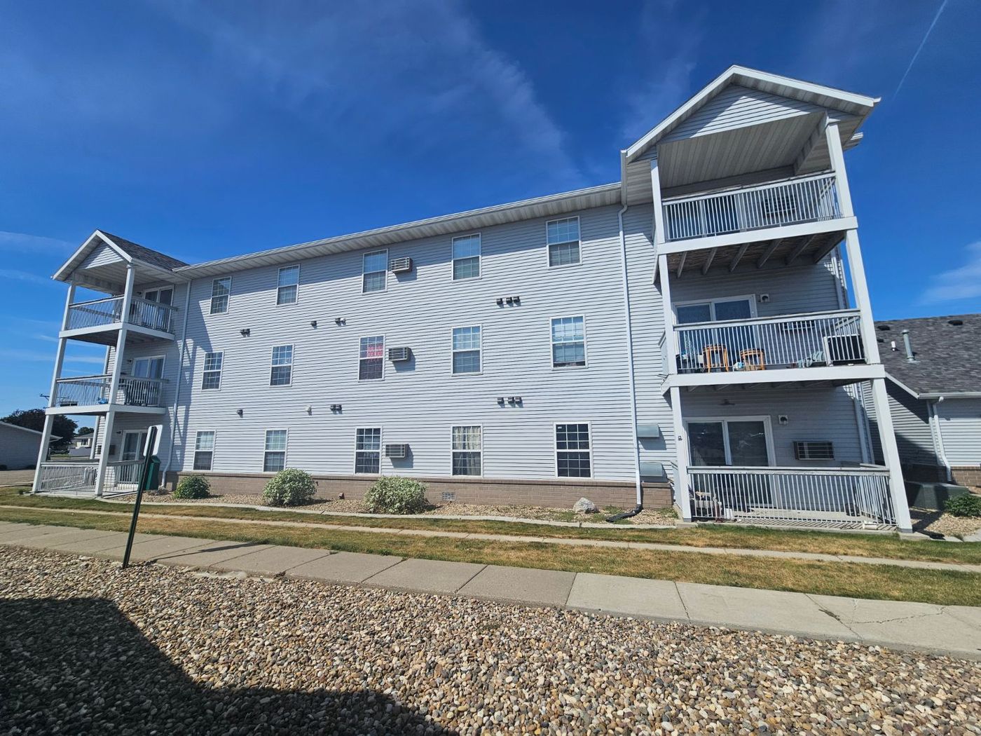 Side elevation of a three-story apartment building with balconies and vinyl siding